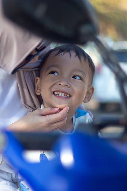 Mother and son are sitting on a motorcyle all terrain vehicle looking at the camera parked on the beach with a bright summer sky.