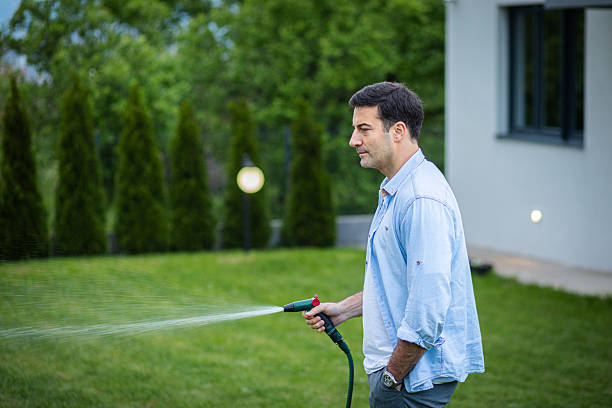 Man is watering his plants with garden hose in his backyard
