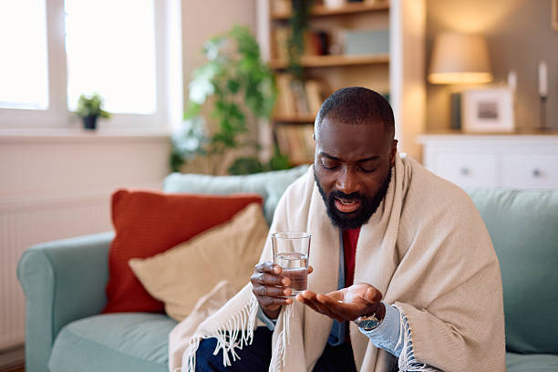 istock Sick african american man taking medicine at home 2224872308