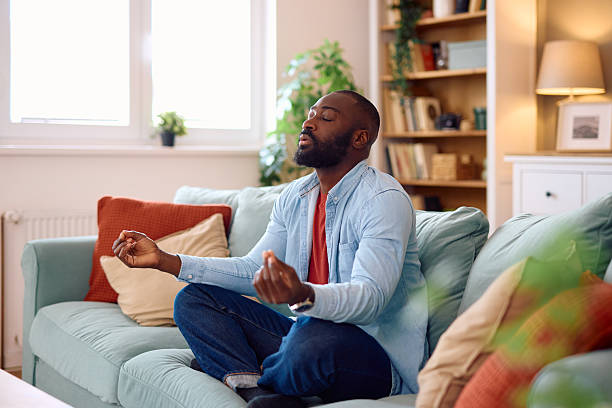 istock Serene man meditating on sofa in cozy living room 2224872311