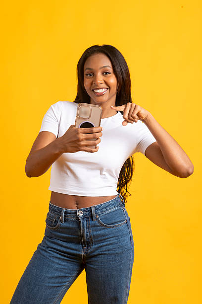 istock Smiling model pointing at smartphone on yellow background 2224876371