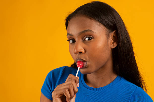 istock Model savoring red lollipop on vibrant yellow backdrop 2224876405