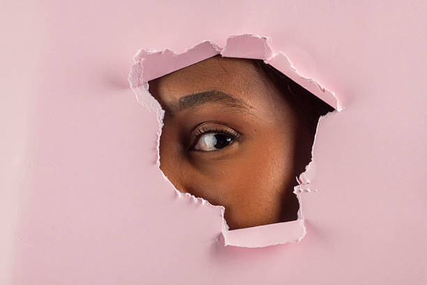 istock Curious black model peeking through torn pink paper 2224877120