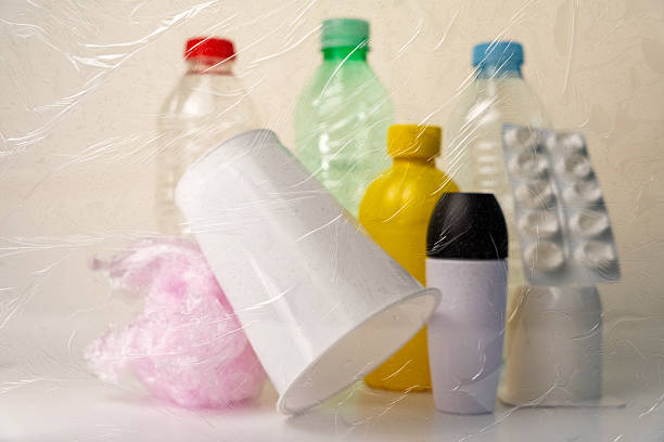 Plastic waste layering — disposable containers, packaging, scattered behind transparent film highlighting environmental contamination problem