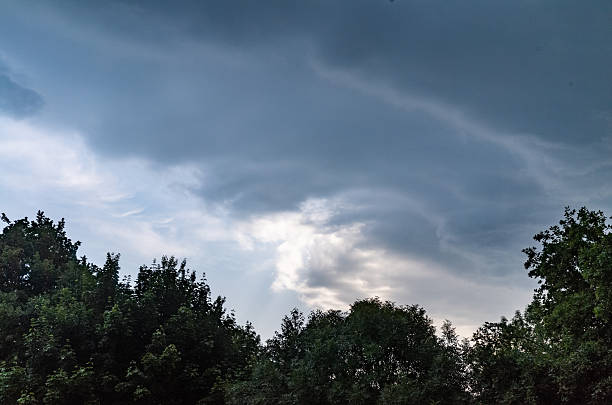 A sky filled with rolling thunderstorm clouds, and the sun is shining through them,  in front of trees. North Rhine-Westphalia, Germany