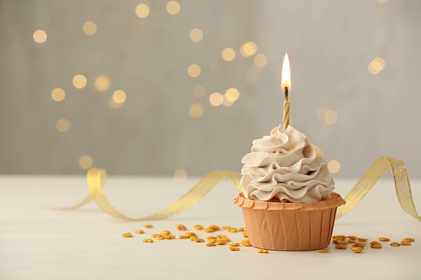 istock Birthday cupcake with burning candle on light table against blurred lights. Space for text 2224877814
