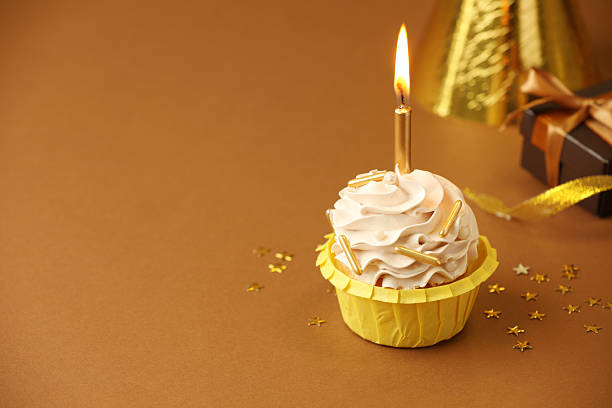 istock Birthday cupcake with burning candle, gift and party cone on brown background. Space for text 2224877823