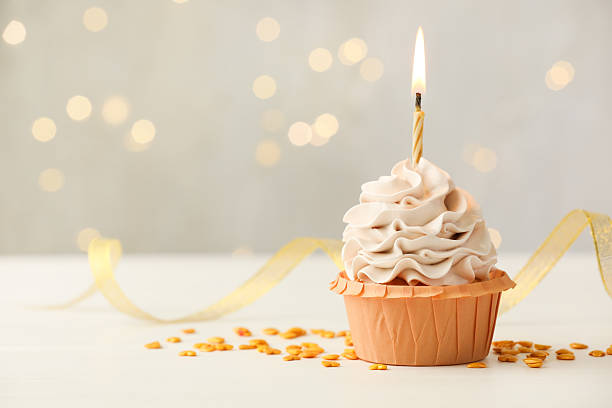 istock Birthday cupcake with burning candle on light table against blurred lights. Space for text 2224877829