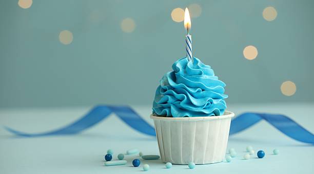 istock Birthday cupcake with burning candle on light blue table against blurred lights. Space for text 2224877846