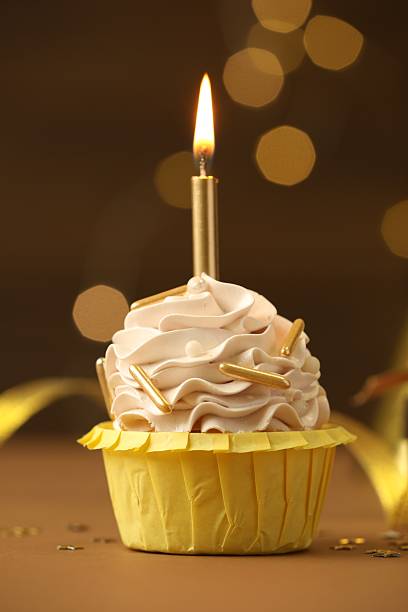 istock Birthday cupcake with burning candle on brown table against blurred lights 2224877848