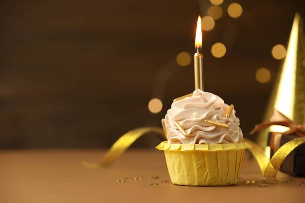 istock Birthday cupcake with burning candle on brown table against blurred lights. Space for text 2224877870