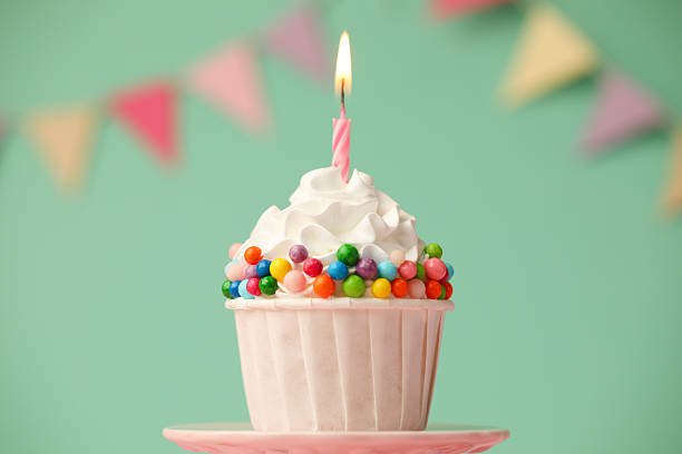 istock Birthday cupcake with burning candle on cake stand against turquoise background 2224877873