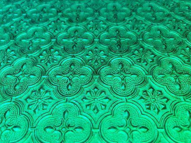 A close-up of translucent glass with an ornate, repeating pattern in vibrant shades of green and turquoise.