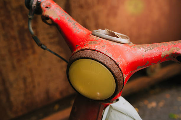 Close-Up View of a Rusty Red Bicycle Handle with Vintage Bell in Urban Setting.