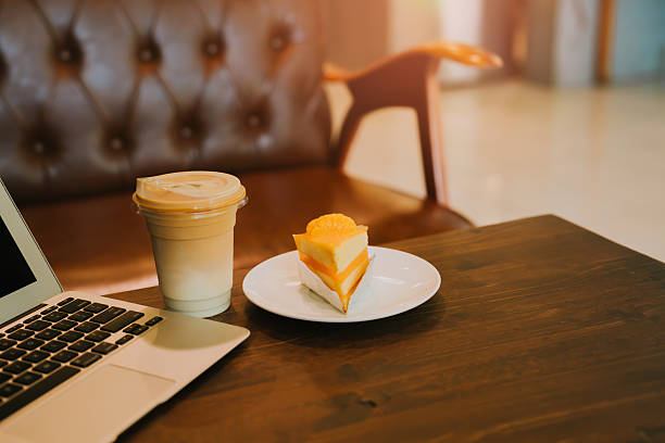 Cozy Coffee Shop Setting with Laptop, Refreshing Drink, Bright Cake Slice, and Comfortable Armchair.