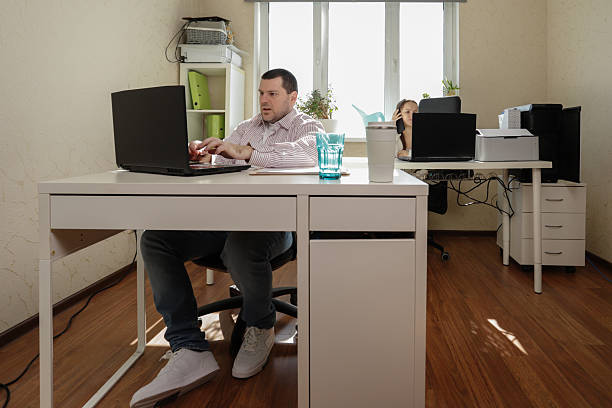 istock Productive home office moment featuring a focused man juggling a phone call and computer work, while his female teammate reaches for the printer tray beside her organized desk setup 2224887974