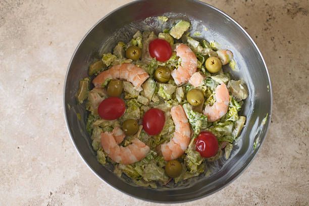 Salad with shrimp, avocado, tomatoes, green lettuce in a glass goblet, a plate against the background of blue linen tablecloth