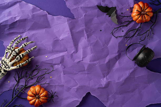 istock Skeleton hand, black branches, pumpkins, and a cauldron highlight this Halloween scene on purple 2224893365