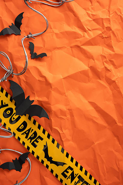 Halloween-themed vertical setup featuring black bats, barbed wire, and caution tape on a crinkled orange surface, evoking a spooky atmosphere ideal for seasonal designs or party invitations