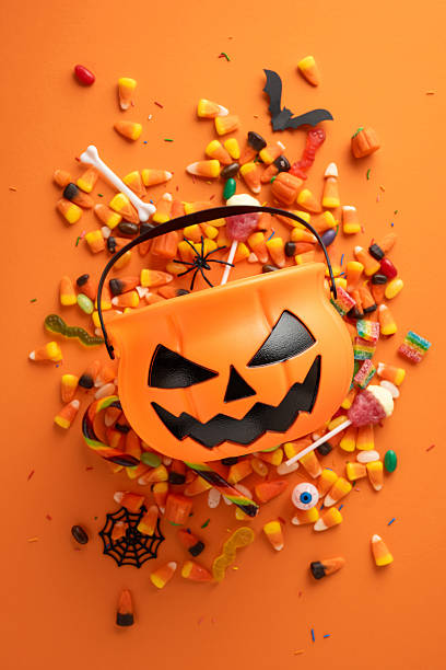 Halloween-themed vertical image featuring an orange pumpkin bucket surrounded by candy and decorations, ideal for seasonal holiday designs