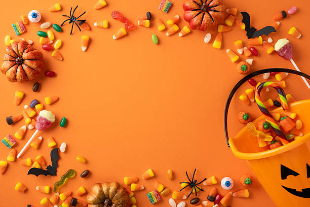 istock Halloween-themed assortment of candy and decorations on an orange surface featuring pumpkins and spiders 2224893409