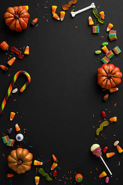 istock Colorful vertical Halloween candy, decorations, and mini pumpkins forming a border on a dark surface 2224893418