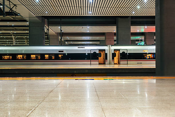 A green high-speed train pulls into a contemporary train station surrounded by electrical infrastructure