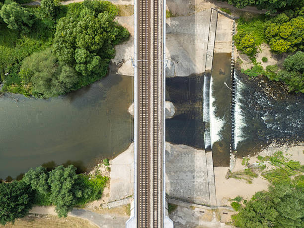 A railway bridge crosses over a river, surrounded by lush greenery. Below, a small waterfall cascades into tranquil waters, showcasing the harmony of nature and infrastructure.A stunning aerial view captures a historic railway bridge gracefully spanning over dense trees and a winding road. The vibrant green landscape highlights the rich natural beauty of the area.An elevated rail bridge, constructed of wood and steel, stretches over a vibrant green valley surrounded by dense trees, reflecting impressive engineering against a bright, clear sky.