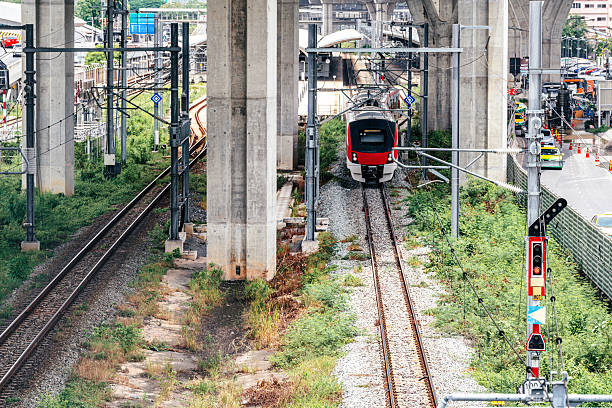 A white and red commuter train moves along elevated tracks surrounded by concrete pillars and greenery