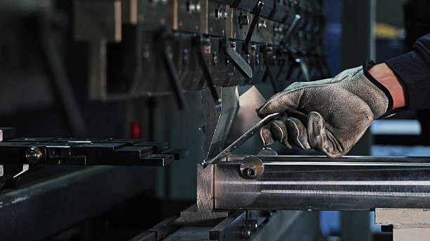 Sheet metal bending on CNC machine. Gloved worker bending a metal sheet using a CNC press brake in an industrial setting focused on precision manufacturing