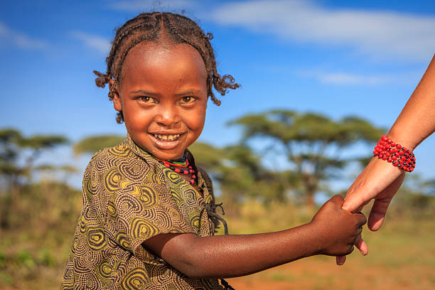 Young caucasian female volunteer holding hand of african child's hand in Ethiopian village.