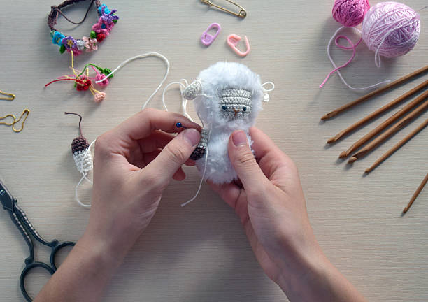 istock Handmade soft toy process with hands knitting small plush animal using crochet hook wool yarn, creative hobby craft table scene close up step by step DIY project, Step 2 - to sew all details of toy 2224906683