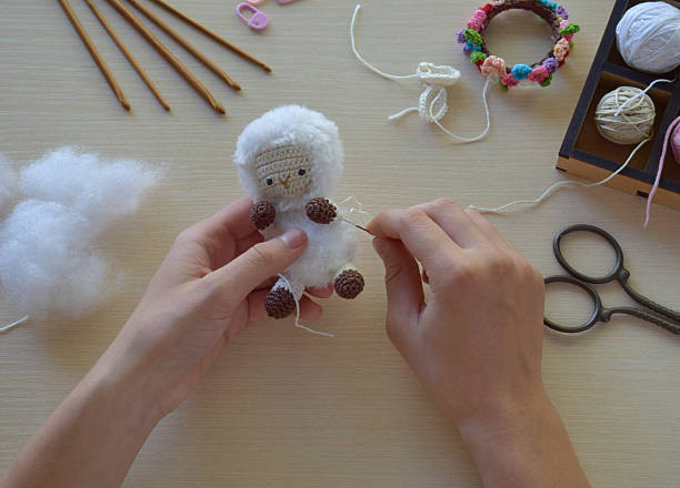 istock Assembling amigurumi sheep toy with white wool and brown feet using crochet and needle by hand DIY process on table handmade crafting close up, Step 2 - to sew all details of toy 2224906695
