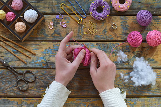 istock Hands crocheting pink yarn creating handmade amigurumi toy using hook on wooden table surrounded by balls of wool scissors and fiber stuffing creative crafting process, Step 1 knit all details of toy 2224906741