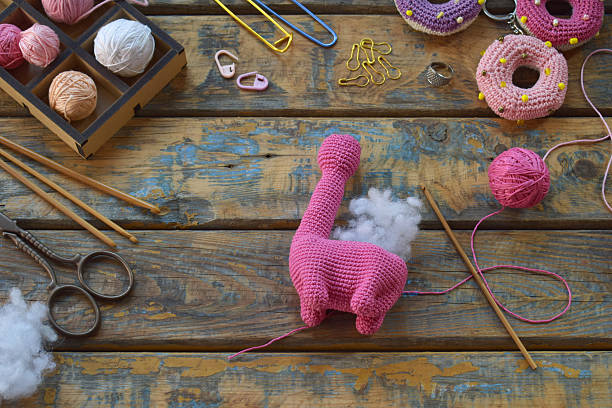 istock finished pink amigurumi dinosaur toy standing on table with wool yarn stuffing scissors crochet tools visible during creative handmade craft process, Step 2 - Stuff toy with padding polyester 2224906742