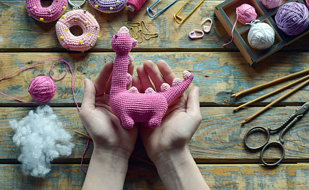 istock Hands holding pink amigurumi dinosaur body with yarn and stuffing preparing for final assembly of handmade toy creative crochet project work in progress 2224906816