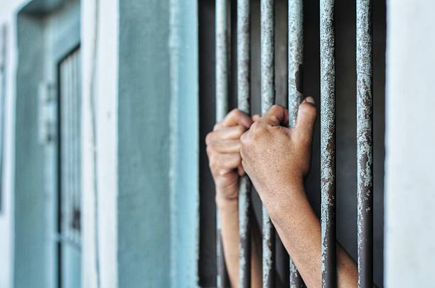 istock hands of a prisoner behind prison bars on black background 2224911484