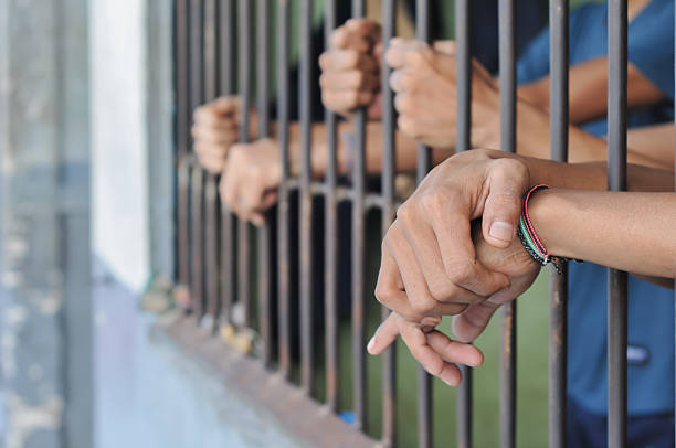 istock hands of a prisoner behind prison bars on black background 2224911564