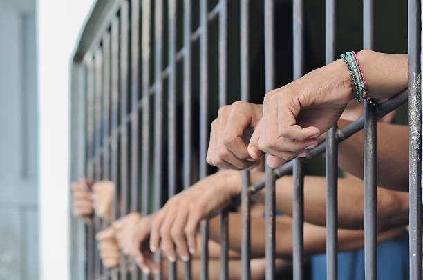 istock hands of a prisoner behind prison bars on black background 2224911623