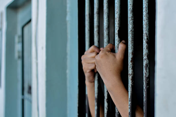 istock hands of a prisoner behind prison bars on black background 2224911699