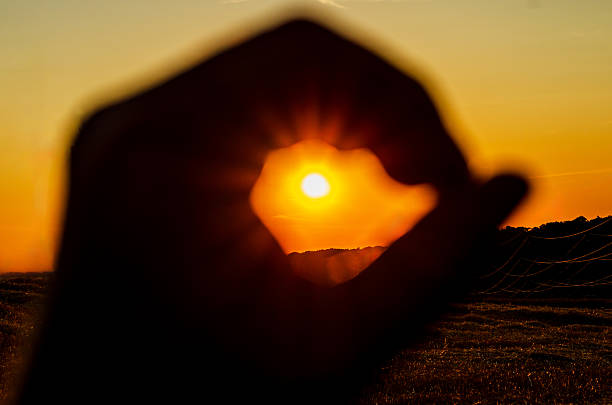 Setting sun framed by silhouette of hand making OK sign against orange sky background