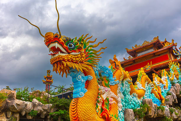 Vibrant golden dragon sculpture against cloudy sky at asian temple complex.