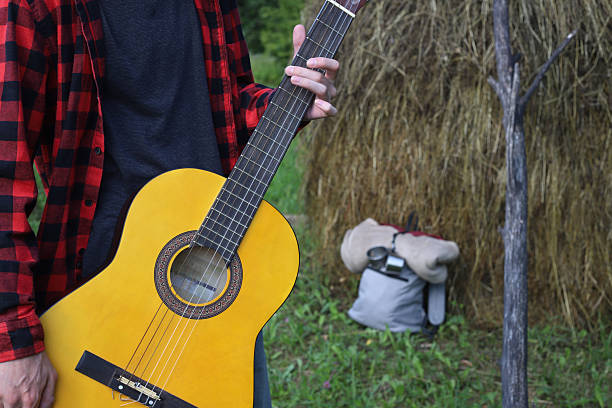 A young guy in a red shirt and jeans with a guitar travels alone through green mountains and nature.