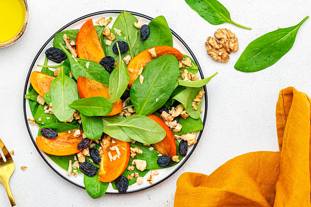 istock Yummy persimmon salad with walnuts, raisin and fresh spinach, white background, top view 2224930243