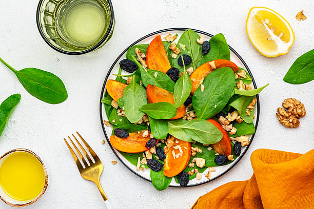 istock Autumn vegan persimmon salad with walnuts, blue raisin and spinach, white background, top view 2224930252