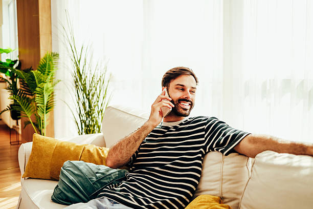 istock Young man relaxing on sofa, talking on mobile phone and smiling 2224933068