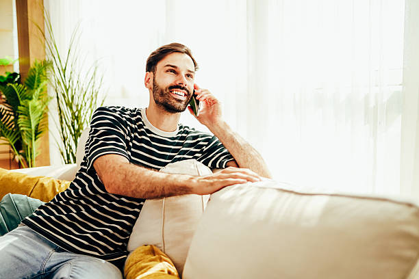 istock Young man relaxing on sofa and talking on mobile phone 2224933071