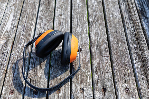 Orange and black ear protection headphones rest on weathered wooden planks, symbolizing safety in loud work environments or outdoor tasks.