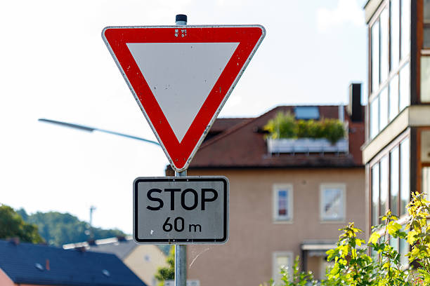 A yield sign with an additional notice indicating a stop in 100 meters, placed along a rural road in an autumn landscape. The sign stands against a backdrop of colorful foliage and open fields, creating a serene countryside setting.