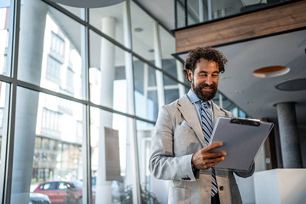 istock Smiling businessman reading notes on clipboard in office lobby 2224952674